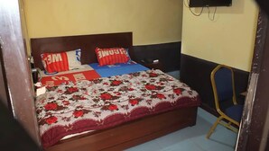 Een slaapkamer met een bed, een stoel, een televisie en een ventilator.