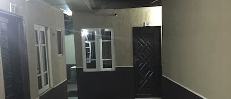 Un pasillo con suelo de baldosas, una puerta con diseño geométrico y un ventanal con marco blanco.