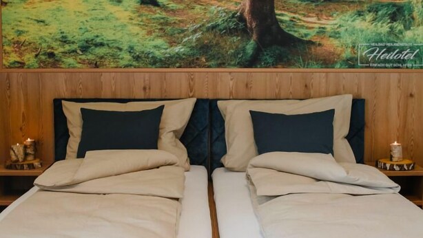 A double bed with a wooden headboard and two bedside tables, each with a candle. - Heilotel (Heilbad Heiligenstadt)