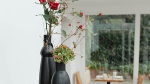 A café with wooden tables and chairs, black vases with flowers, and a tiled floor. - Heilotel (Heilbad Heiligenstadt)