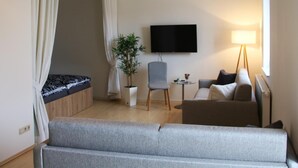 A modern hotel room with a bed, a sofa, a chair, a small table, a potted plant, a TV, and a lamp. - Heilotel (Heilbad Heiligenstadt)