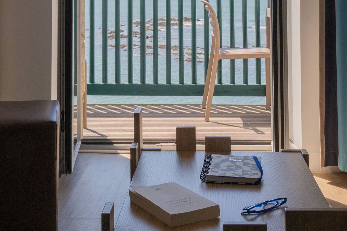 Une pièce avec une table en bois, une chaise et une vue sur la plage depuis un balcon.