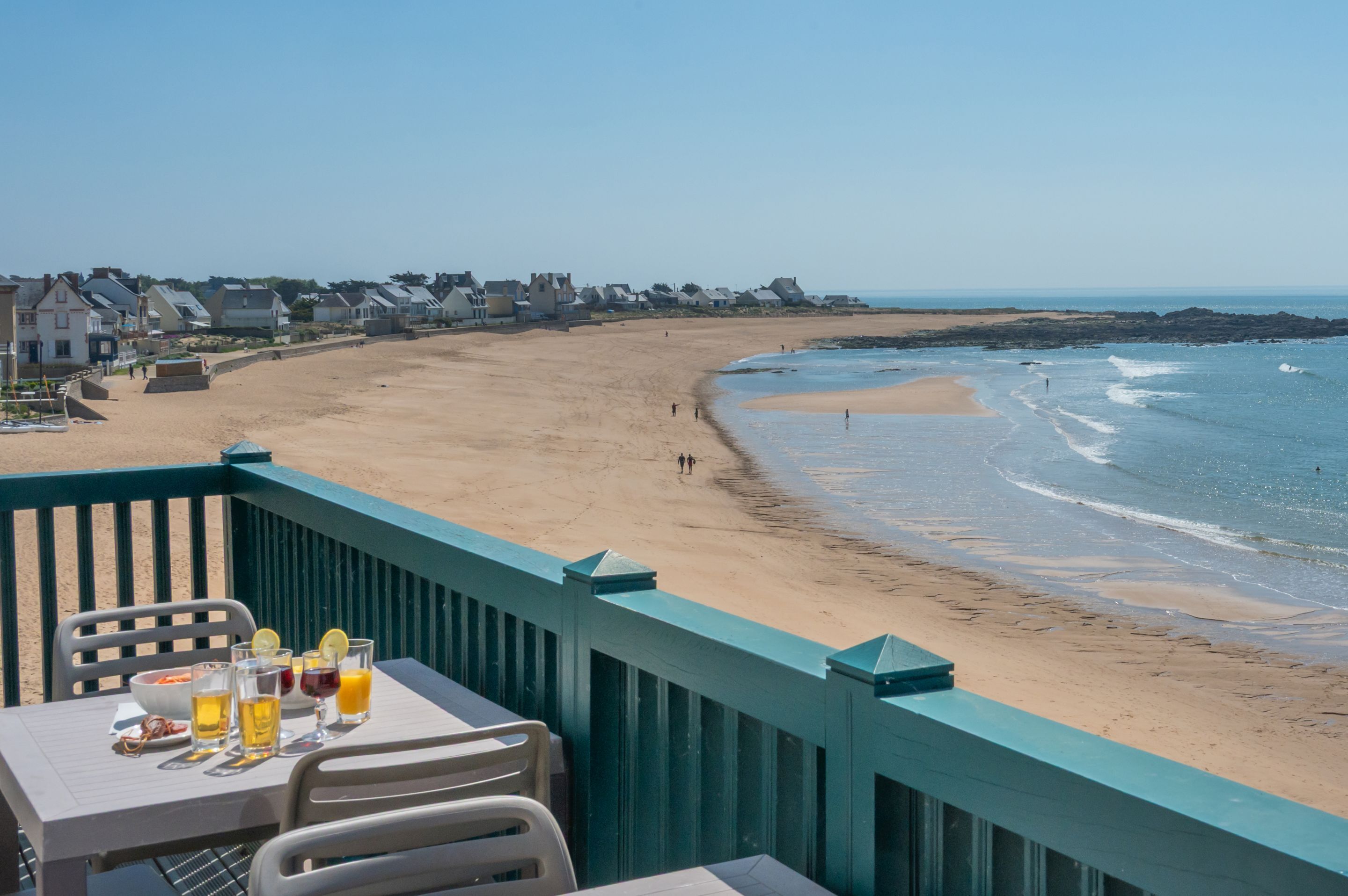 Vista a la playa desde un balcón con una mesa para dos, con vista a una playa arenosa y al océano.