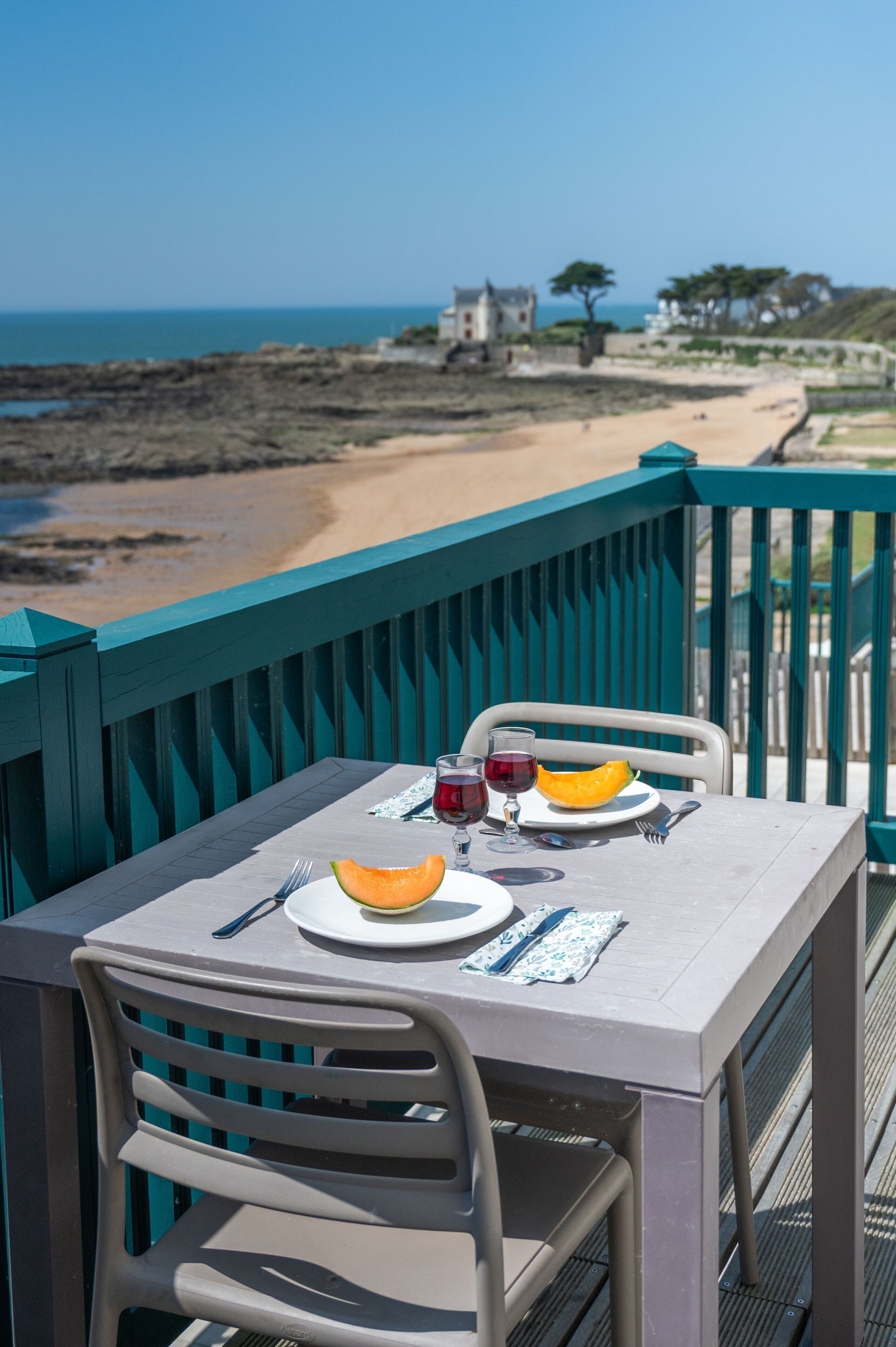 Une table avec une assiette de nourriture et des boissons, une chaise, et une vue sur la plage et l’océan.