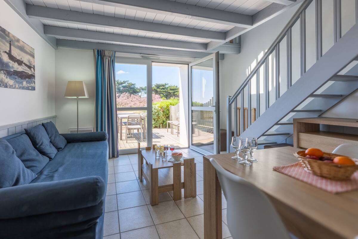 Un salon moderne avec un canapé, une table à manger et des chaises. Un escalier mène à un niveau supérieur.
