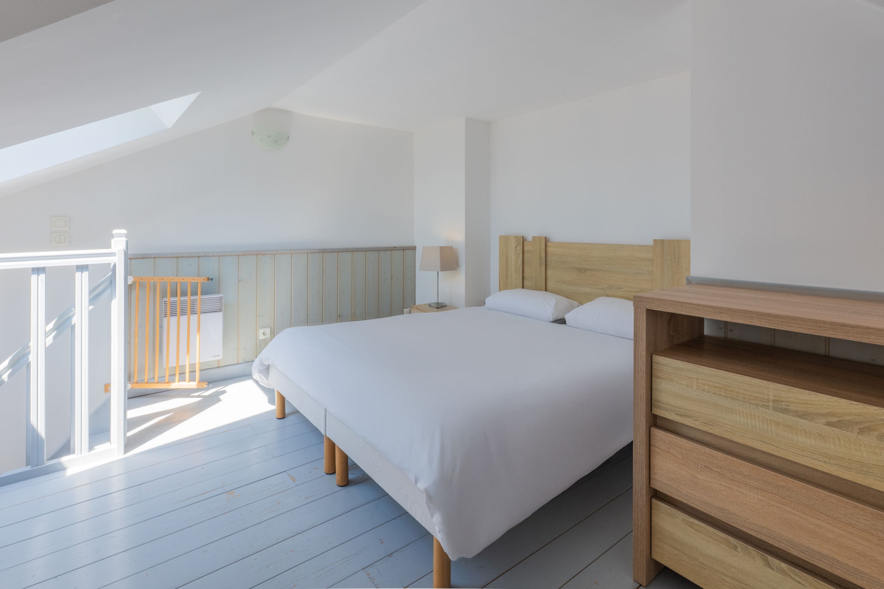 Une chambre à coucher avec un cadre de lit en bois, un matelas blanc et une table de chevet avec une lampe.
