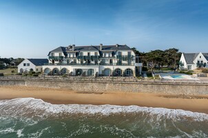 Um edifício grande e com vários andares, com varanda, situado perto de uma praia arenosa com ondas.