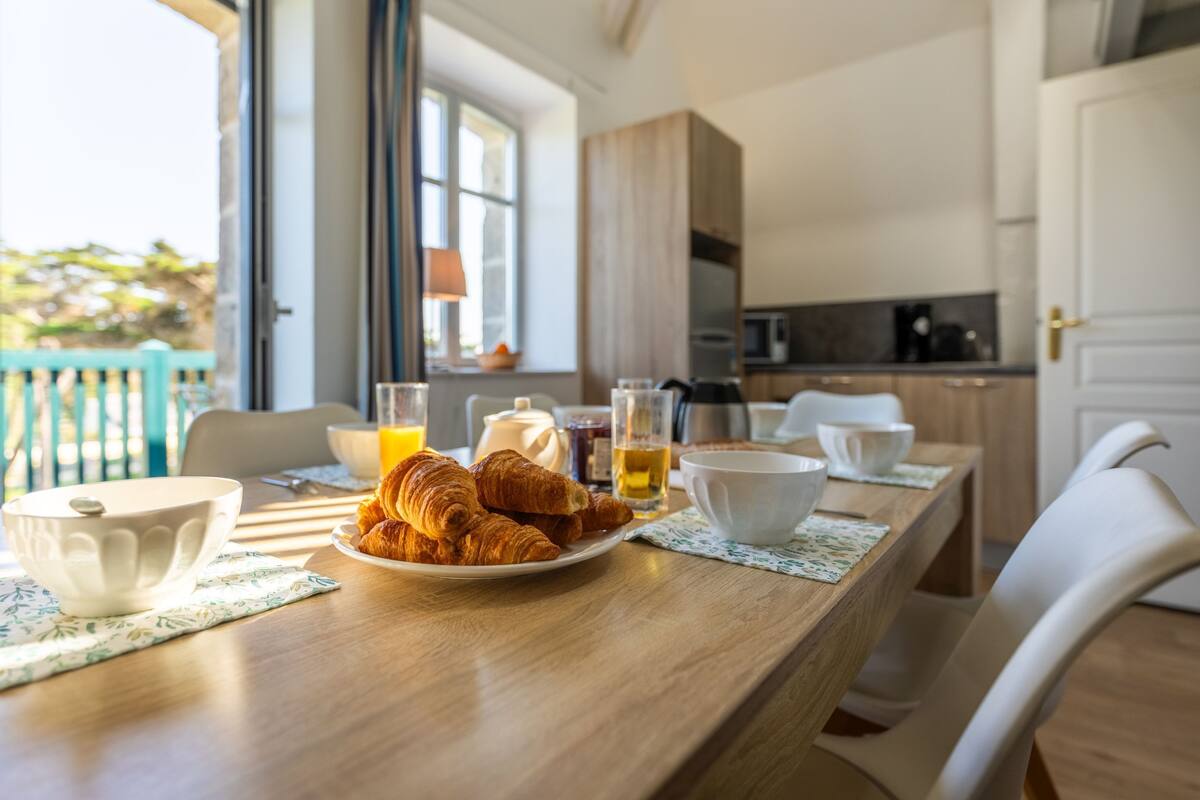 Une table de petit-déjeuner avec des croissants, un bol et un verre de jus d’orange.