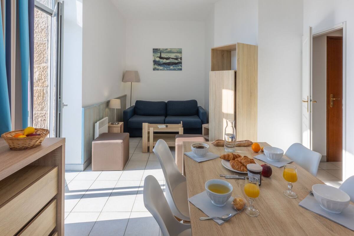 Un salon moderne avec un canapé, une table à manger dressée pour le petit-déjeuner et une vue sur l’extérieur.