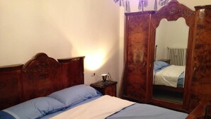 A bedroom with a wooden bed, a nightstand with a lamp, and a full-length mirror. - Apartment in southern Milan Melegnano (Melegnano)