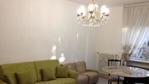 A living room with a green sofa, a beige sofa, a dining table with chairs, and a chandelier. - Apartment in southern Milan Melegnano (Melegnano)