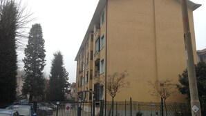 A multi-story yellow building with a gated entrance, parked cars, and a fenced area with trees. - Apartment in southern Milan Melegnano (Melegnano)
