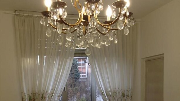 A dining room with a round table, chairs, a chandelier, and a window with curtains. - Apartment in southern Milan Melegnano (Melegnano)