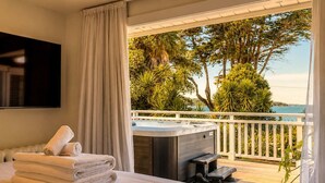 Una camera da letto con un letto, una vasca idromassaggio e un balcone vista alberi e mare.