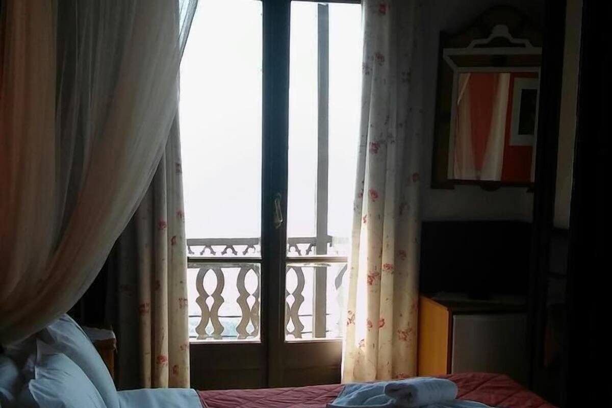 A hotel room with a bed, a desk, a chair, and a balcony with a railing.