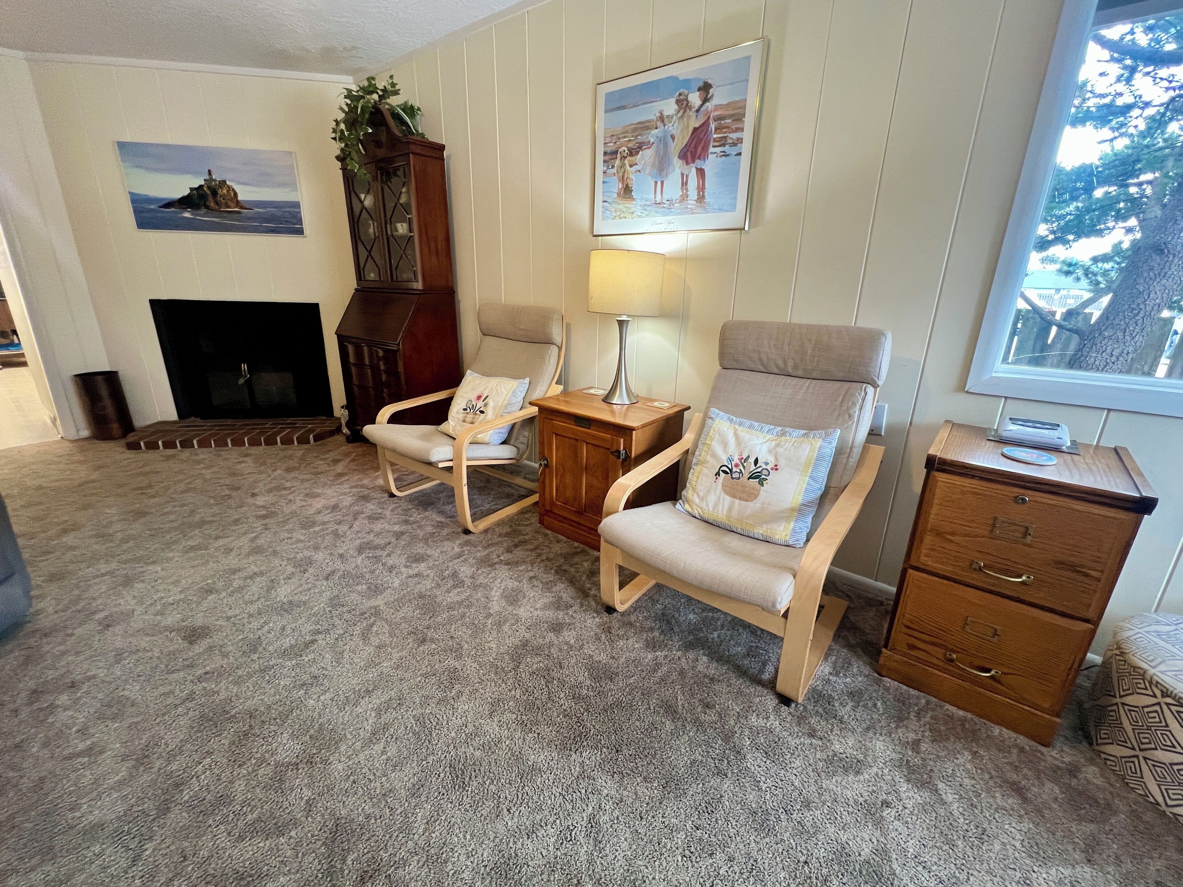 A living room with two armchairs, a wooden cabinet, a fireplace, and a framed picture on the wall.