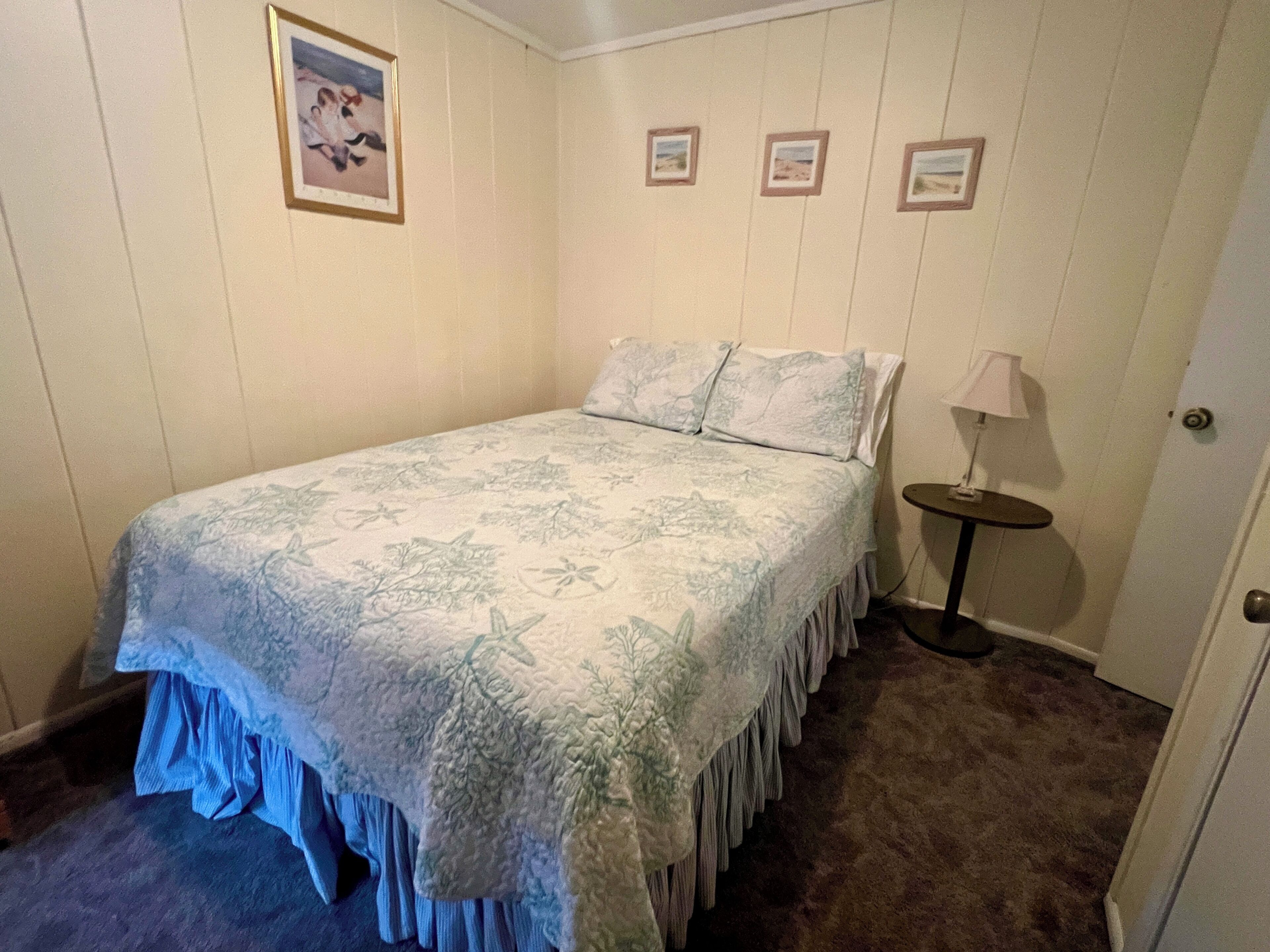 A bedroom with a bed, a nightstand, a lamp, and framed pictures on the wall.