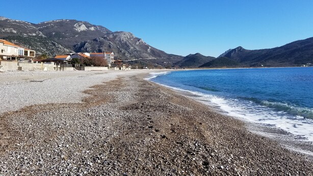 A pebbled beach with buildings and mountains in the background. - Aparthotel Monterria (Bar)