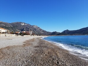 A pebbled beach with buildings and mountains in the background. - Aparthotel Monterria (Bar)