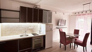 A modern kitchen with dark cabinets, a white countertop, and a dining area with a table and chairs. - Aparthotel Monterria (Bar)