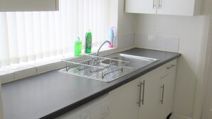 A compact kitchen with a washing machine, a sink, and a window with blinds.