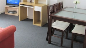 A room with a wooden desk, a computer, a chair, a table, and a painting on the wall.