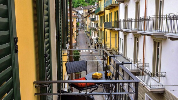 Un balcone con tavolo e sedie, affaccia su una strada con edifici e una montagna sullo sfondo.