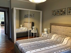 Quarto com cama, mesas de cabeceira, guarda-roupa e quadros nas paredes.