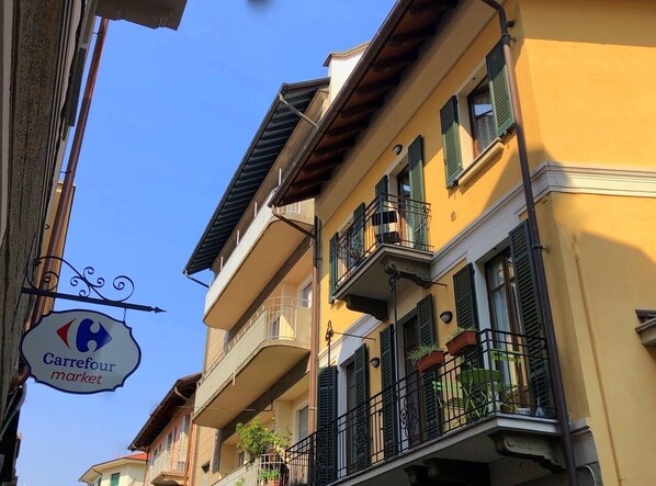 Um edifício de vários andares com varandas, um letreiro visível da 'Carrefour market', e um céu azul claro.