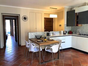 Cozinha moderna com armários brancos, mesa de jantar de madeira e cadeiras brancas.