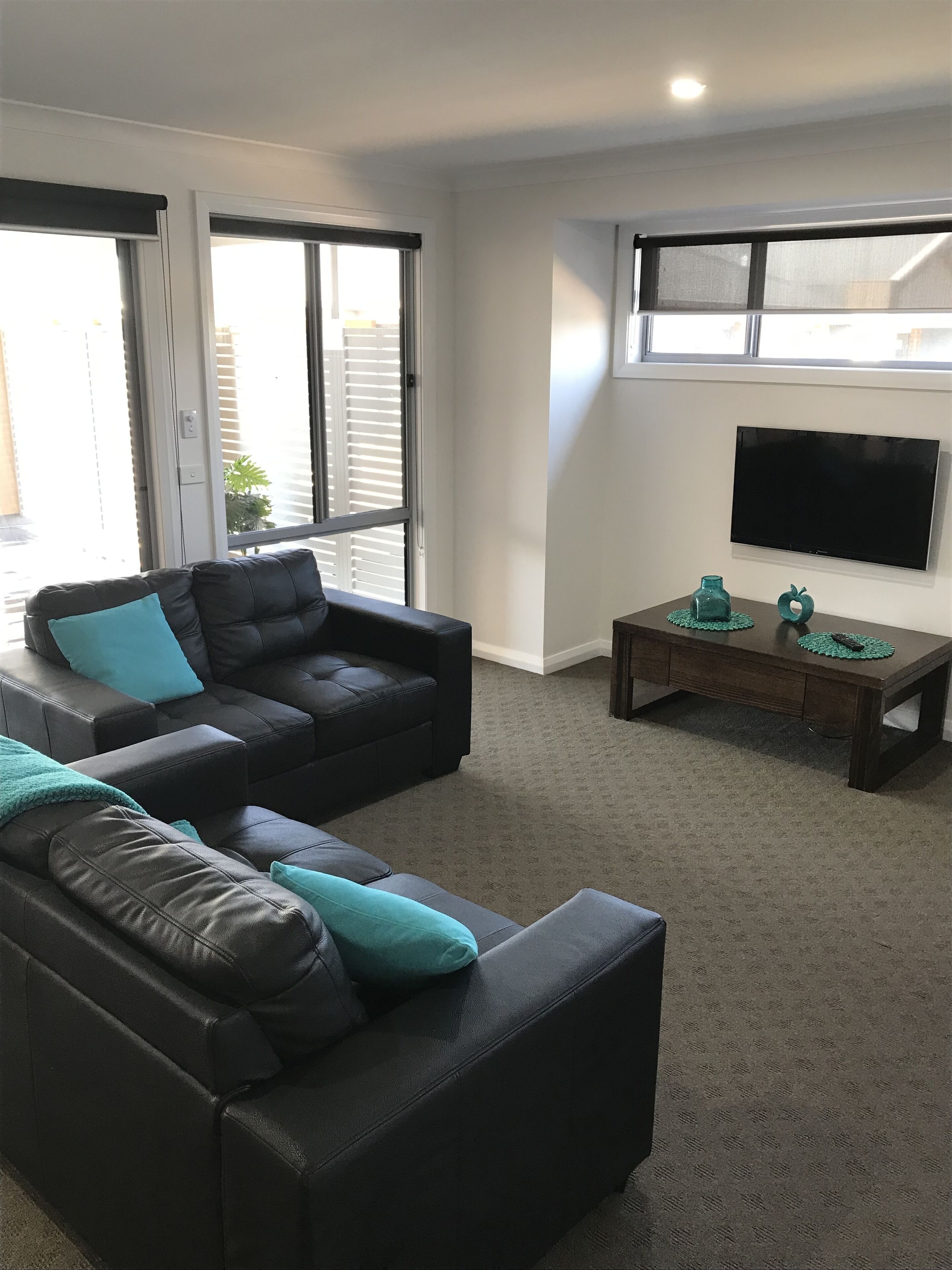 A living room with a sectional sofa, a coffee table, and a flat-screen TV mounted on the wall.