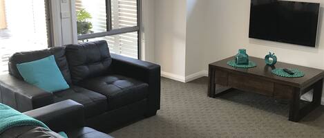 A living room with a sectional sofa, a coffee table, and a flat-screen TV mounted on the wall.