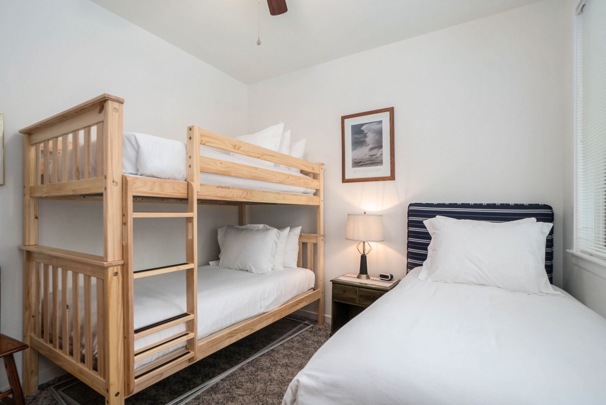 A bunk bed room with a wooden headboard, a bedside table with a lamp, and a framed picture on the wall.