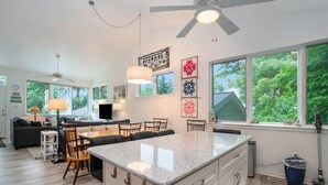 Cocina moderna con una isla central, comedor con sillas y un amplio ventanal con vistas a zonas verdes.