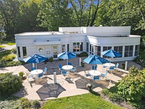A white building with a patio area featuring outdoor seating and blue umbrellas. - Sleepy Hollow Beach Resort introduces Patio 33 (South Haven)