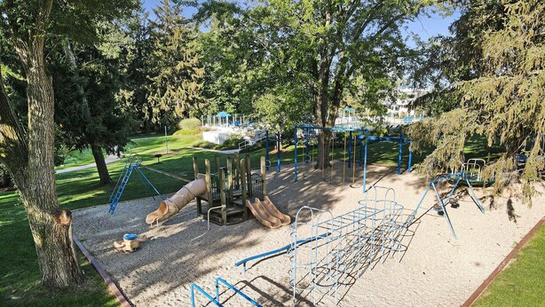 Un parque infantil con diversas estructuras de juego, como toboganes y columpios, rodeado de árboles y césped.