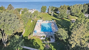Vista aérea de una propiedad con piscina rodeada de árboles, vistas despejadas al mar y un césped bien cuidado.
