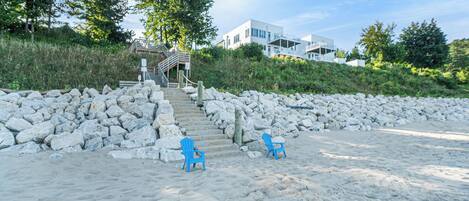 A beach with two blue chairs, a stone wall, and a staircase leading to a building.
