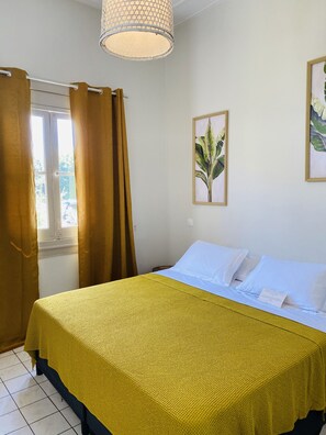 Una habitación con una cama, una ventana con cortinas, una lámpara colgante y una planta enmarcada en la pared.