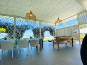 Un espacio de comedor al aire libre con techo, mobiliario de mimbre e iluminación colgante, con vistas a un paisaje pintoresco.