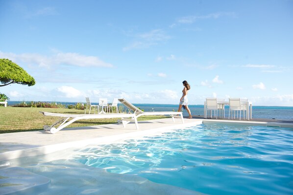 Un área de piscina con sillones de descanso y vista al océano.