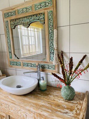 Un baño con un lavamanos blanco, un jarrón verde con plantas secas y un espejo con un marco verde ornamentado.