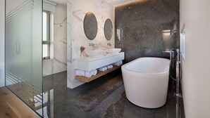 A modern bathroom with a large freestanding bathtub, a glass shower enclosure, and marble walls. - Elea Silver Villa (Pegeia)