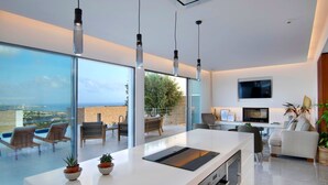 A modern kitchen with a large island, a dining area with chairs, and a living room with a sofa. - Elea Silver Villa (Pegeia)