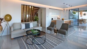 A modern living room with a sofa, armchairs, a coffee table, and a dining area with a kitchen in the background. - Elea Silver Villa (Pegeia)