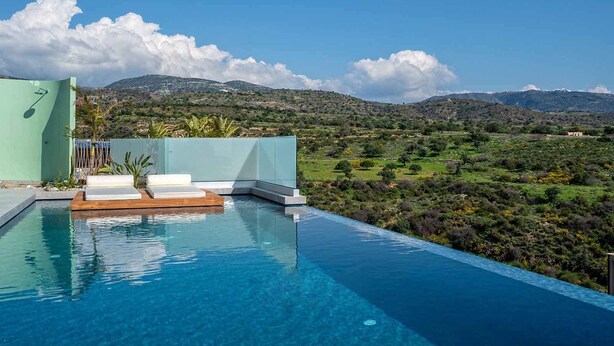 A modern infinity pool with a wooden deck and lounge chairs, overlooking a lush landscape with mountains in the background. - Elea Silver Villa (Pegeia)
