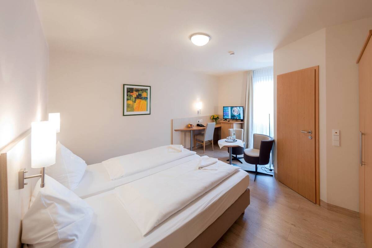 Ein Hotelzimmer mit einem großen Bett, einem Schreibtisch, einem Sessel und einem Fernseher.