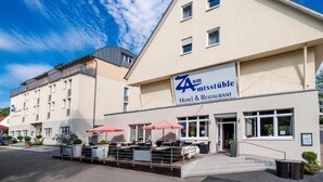 A hotel with a sign reading "Zum Mtsstüble Hotel & Restaurant" and outdoor seating with umbrellas.
