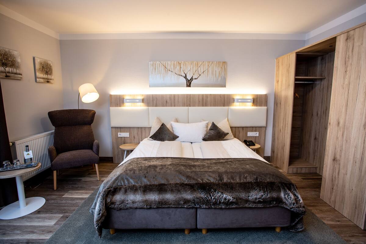 Ein modernes Schlafzimmer mit einem großen Bett, einem Sessel, einem Nachttisch und einer Wandlampe.