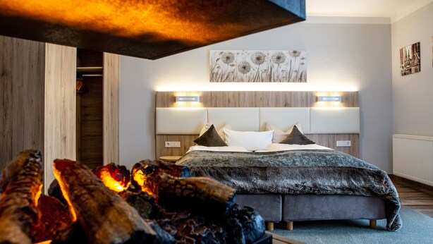 A bedroom with a bed, bedside lamps, a wall-mounted artwork, and a fireplace.
